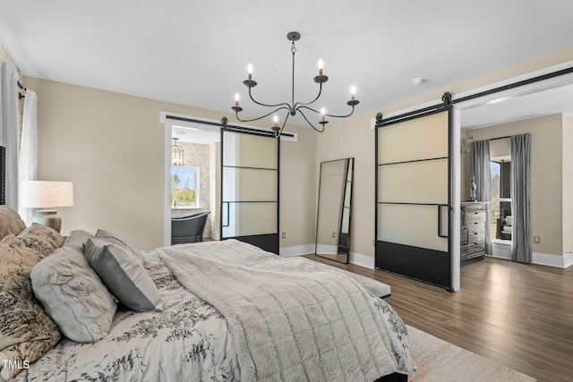 bedroom with an inviting chandelier, baseboards, a barn door, and wood finished floors