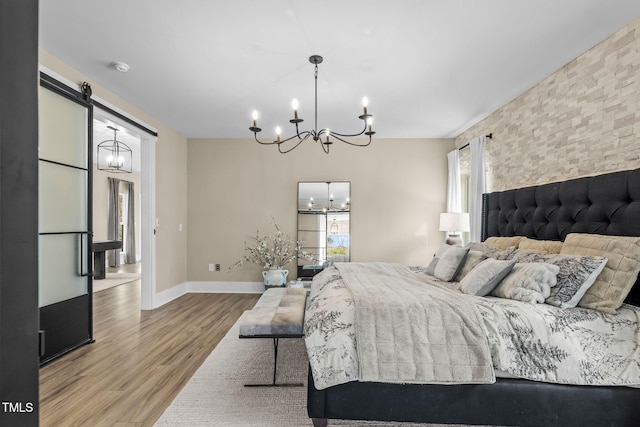 bedroom with an inviting chandelier, multiple windows, wood finished floors, and a barn door