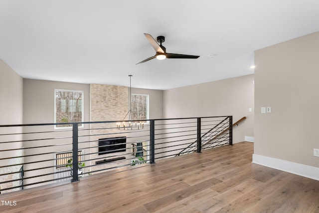 unfurnished room featuring ceiling fan with notable chandelier, wood finished floors, and baseboards