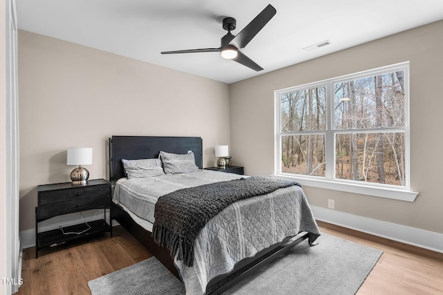 bedroom with ceiling fan, wood finished floors, visible vents, and baseboards