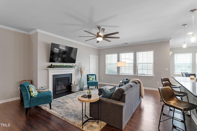 living area featuring a fireplace with flush hearth, dark wood-type flooring, a ceiling fan, crown molding, and baseboards