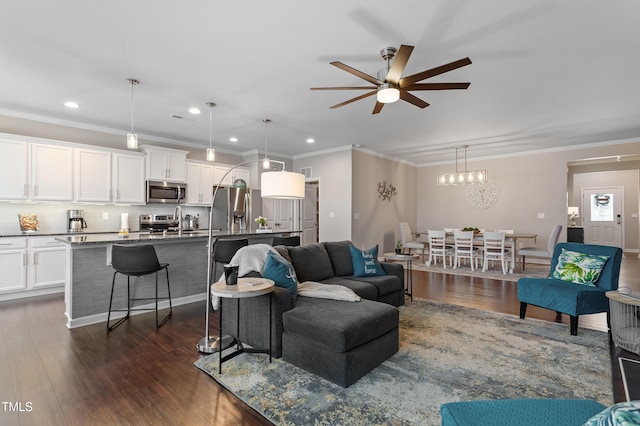 living area featuring recessed lighting, ceiling fan with notable chandelier, dark wood-style flooring, and ornamental molding