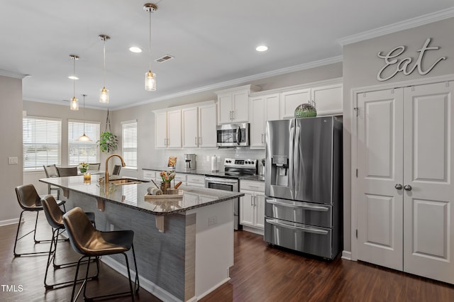 kitchen featuring visible vents, a kitchen island with sink, a sink, ornamental molding, and stainless steel appliances