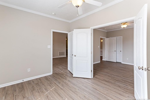 empty room with light wood-type flooring, visible vents, ornamental molding, a ceiling fan, and baseboards