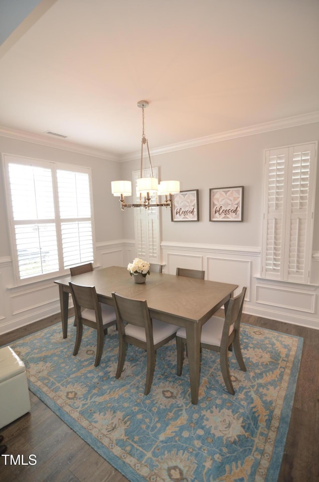 dining area with visible vents, dark wood-style flooring, wainscoting, crown molding, and a notable chandelier