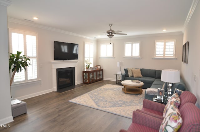 living area featuring a ceiling fan, baseboards, a fireplace with flush hearth, dark wood-style flooring, and crown molding