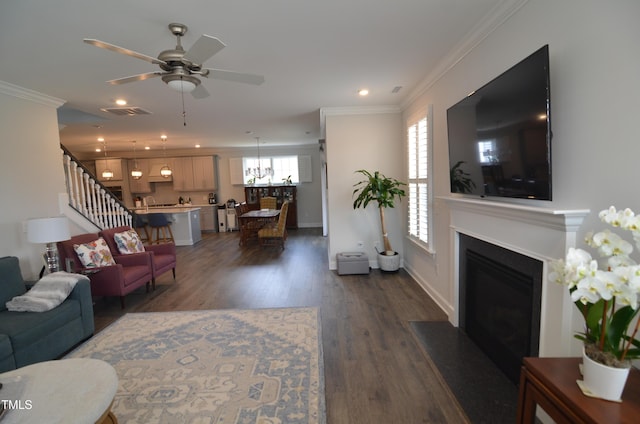 living area with dark wood-type flooring, stairway, a fireplace with flush hearth, and ornamental molding