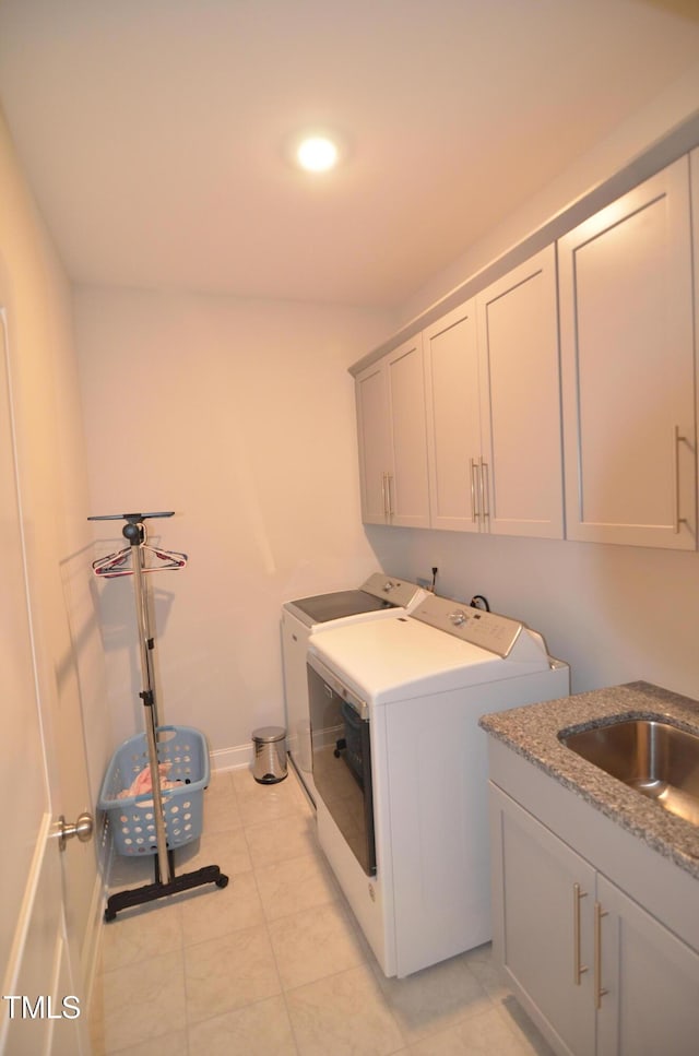 laundry area with baseboards, light tile patterned floors, washer and dryer, cabinet space, and a sink