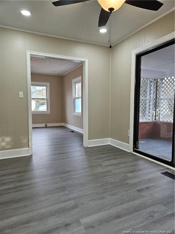 unfurnished room featuring visible vents, dark wood-type flooring, ornamental molding, baseboards, and ceiling fan