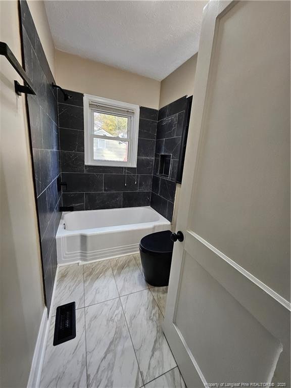 bathroom featuring toilet, marble finish floor, bathing tub / shower combination, and a textured ceiling