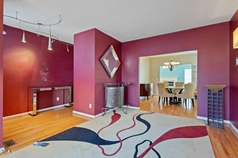 living area featuring baseboards, an accent wall, an inviting chandelier, and wood finished floors