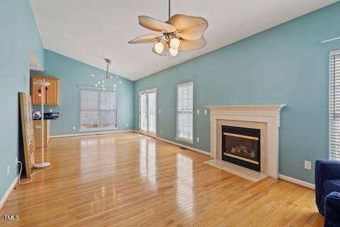 unfurnished living room with baseboards, ceiling fan, a fireplace with flush hearth, lofted ceiling, and wood finished floors