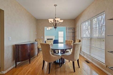 dining area with baseboards, a chandelier, a fireplace, and light wood finished floors