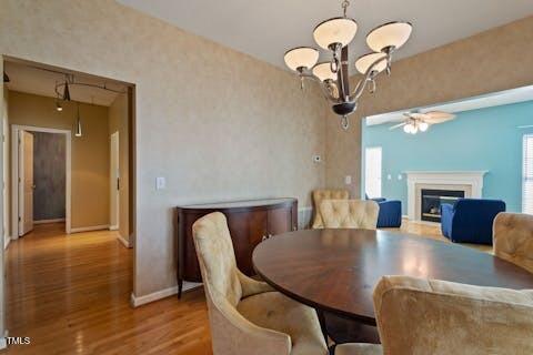 dining area with a glass covered fireplace, ceiling fan with notable chandelier, wood finished floors, and baseboards