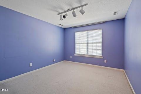 spare room featuring rail lighting, carpet flooring, and baseboards