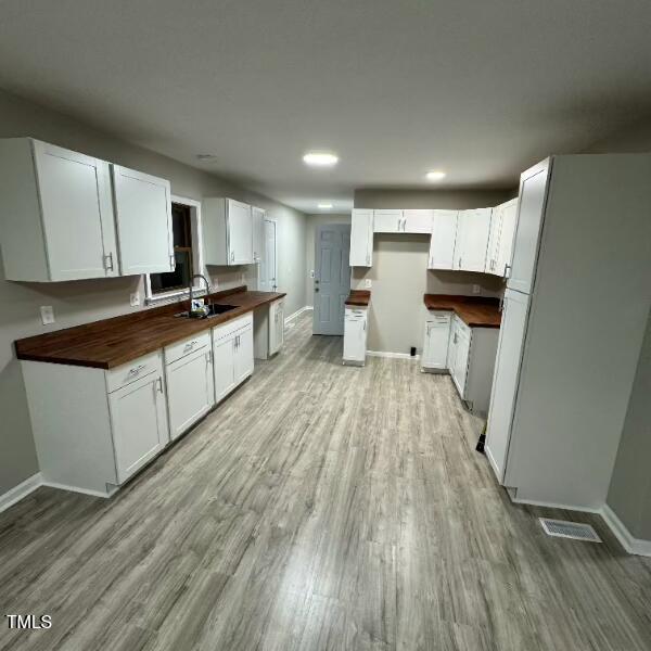 kitchen featuring butcher block countertops, white cabinetry, freestanding refrigerator, light wood finished floors, and baseboards