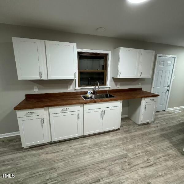 kitchen with light wood finished floors, baseboards, butcher block countertops, white cabinets, and a sink