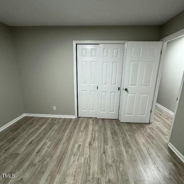 unfurnished bedroom featuring wood finished floors, baseboards, and a closet