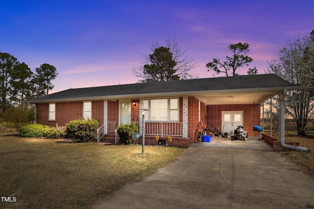 ranch-style house with brick siding, an attached carport, driveway, and a yard