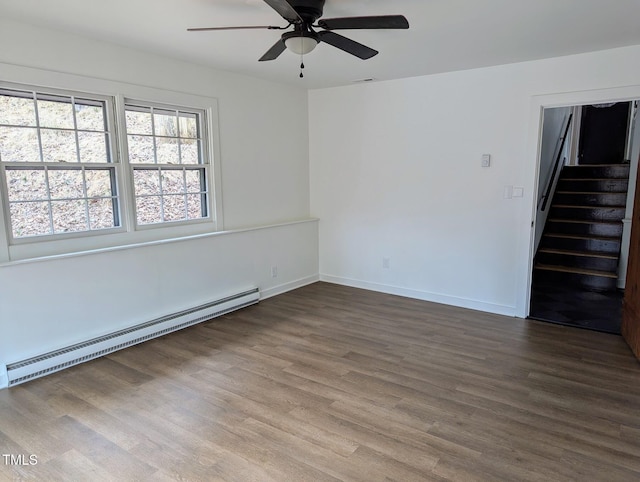 spare room with a ceiling fan, wood finished floors, a baseboard radiator, baseboards, and stairs