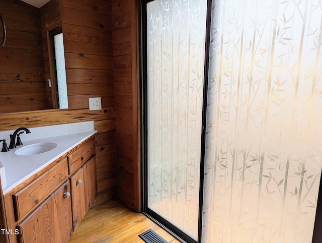 bathroom with visible vents, wood walls, vanity, and hardwood / wood-style flooring