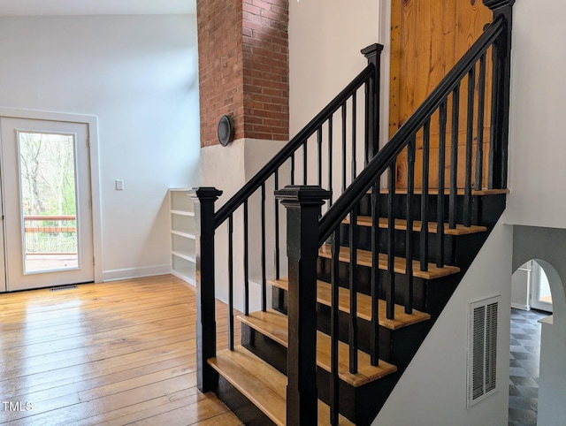 staircase with arched walkways, visible vents, baseboards, and hardwood / wood-style flooring