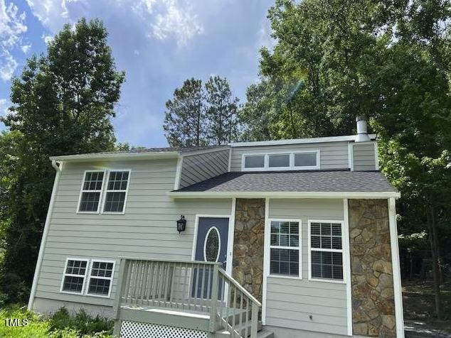 view of front of property with stone siding, a deck, and a shingled roof