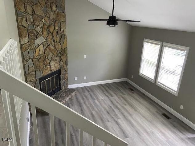 unfurnished living room featuring visible vents, lofted ceiling, a ceiling fan, wood finished floors, and baseboards