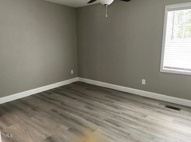 empty room with dark wood finished floors, visible vents, ceiling fan, and baseboards