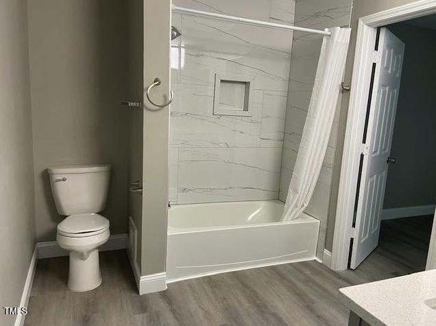 bathroom with baseboards, toilet, wood finished floors, vanity, and shower / bathtub combination with curtain