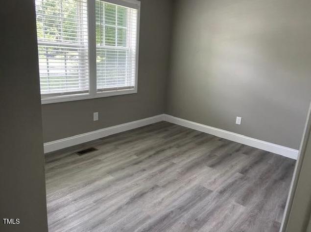 spare room featuring visible vents, baseboards, and dark wood-style floors