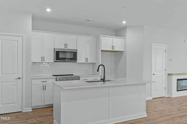 kitchen with stainless steel microwave, light wood-style flooring, stove, white cabinets, and a sink