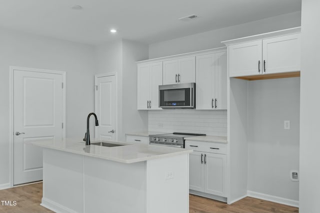 kitchen featuring an island with sink, decorative backsplash, appliances with stainless steel finishes, white cabinets, and a sink