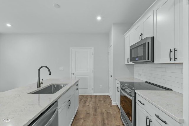 kitchen with light stone countertops, a sink, decorative backsplash, stainless steel appliances, and white cabinetry