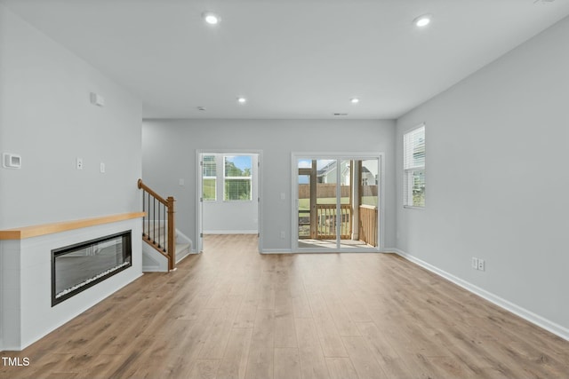 unfurnished living room featuring baseboards, stairway, recessed lighting, light wood-style flooring, and a glass covered fireplace