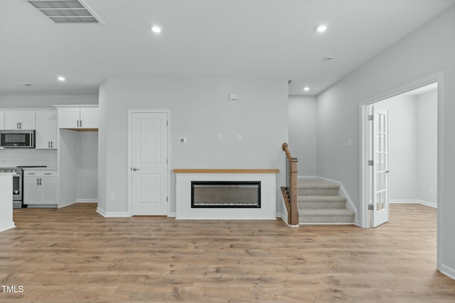 living area featuring visible vents, recessed lighting, stairs, light wood-style floors, and a glass covered fireplace