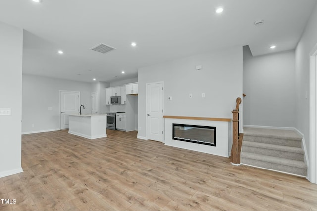 unfurnished living room featuring recessed lighting, visible vents, a glass covered fireplace, and light wood finished floors