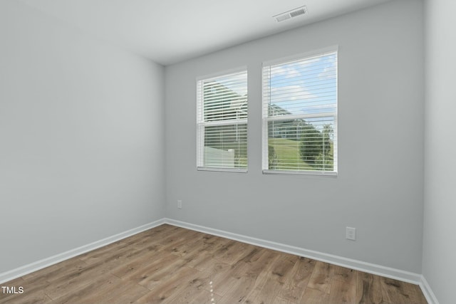 empty room with light wood-style floors, visible vents, and baseboards