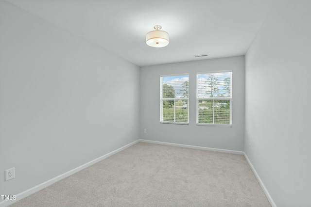 empty room with baseboards, visible vents, and light carpet