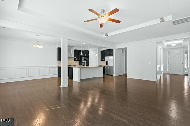 unfurnished living room with ceiling fan with notable chandelier, a raised ceiling, dark wood-type flooring, and ornamental molding