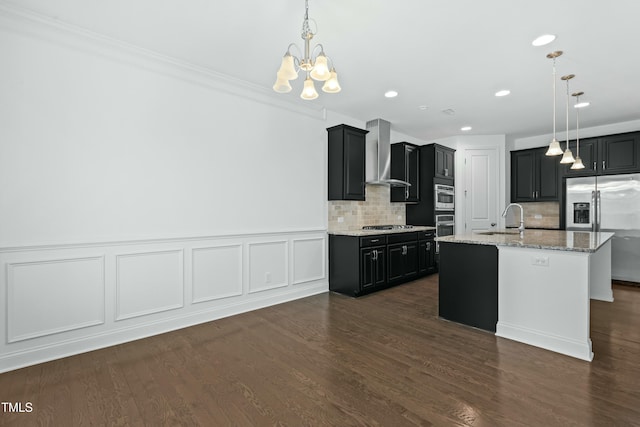 kitchen with a notable chandelier, appliances with stainless steel finishes, dark cabinetry, and wall chimney range hood