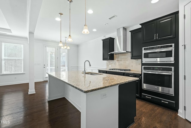 kitchen featuring visible vents, a sink, appliances with stainless steel finishes, wall chimney range hood, and dark cabinets