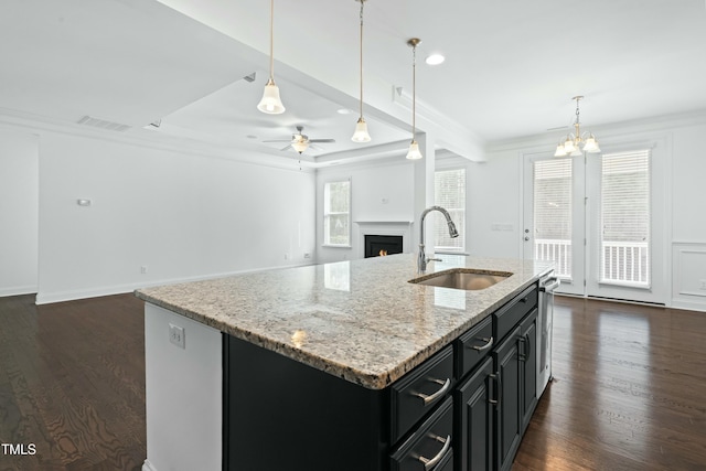 kitchen featuring a sink, a warm lit fireplace, open floor plan, dark cabinets, and dark wood-style flooring