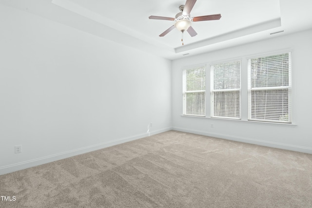 empty room featuring visible vents, light colored carpet, baseboards, and a tray ceiling