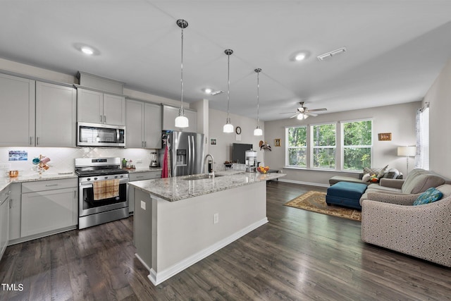 kitchen featuring light stone counters, a sink, open floor plan, appliances with stainless steel finishes, and tasteful backsplash