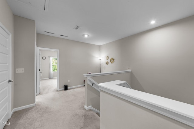 hallway with visible vents, an upstairs landing, light carpet, baseboards, and attic access