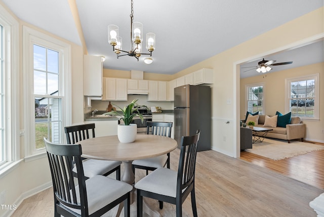 dining room featuring light wood finished floors, a healthy amount of sunlight, ceiling fan with notable chandelier, and baseboards