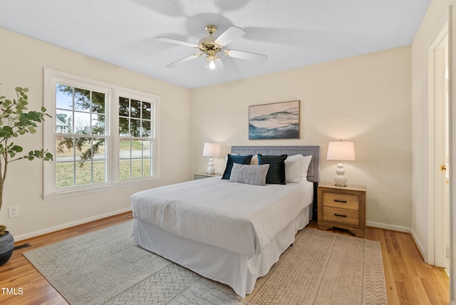 bedroom with a ceiling fan, visible vents, baseboards, and light wood finished floors