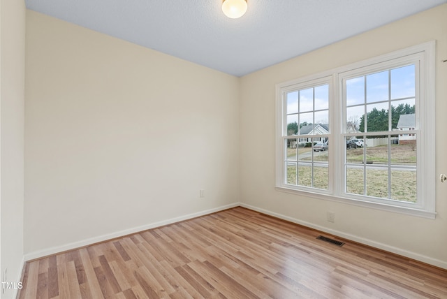 unfurnished room featuring visible vents, light wood-type flooring, and baseboards