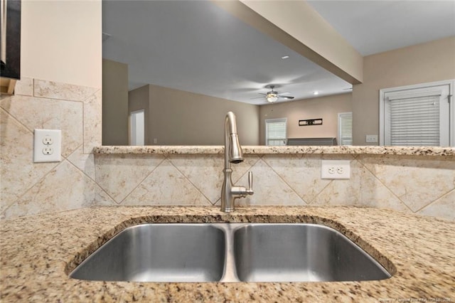 kitchen with ceiling fan, light stone counters, tasteful backsplash, and a sink